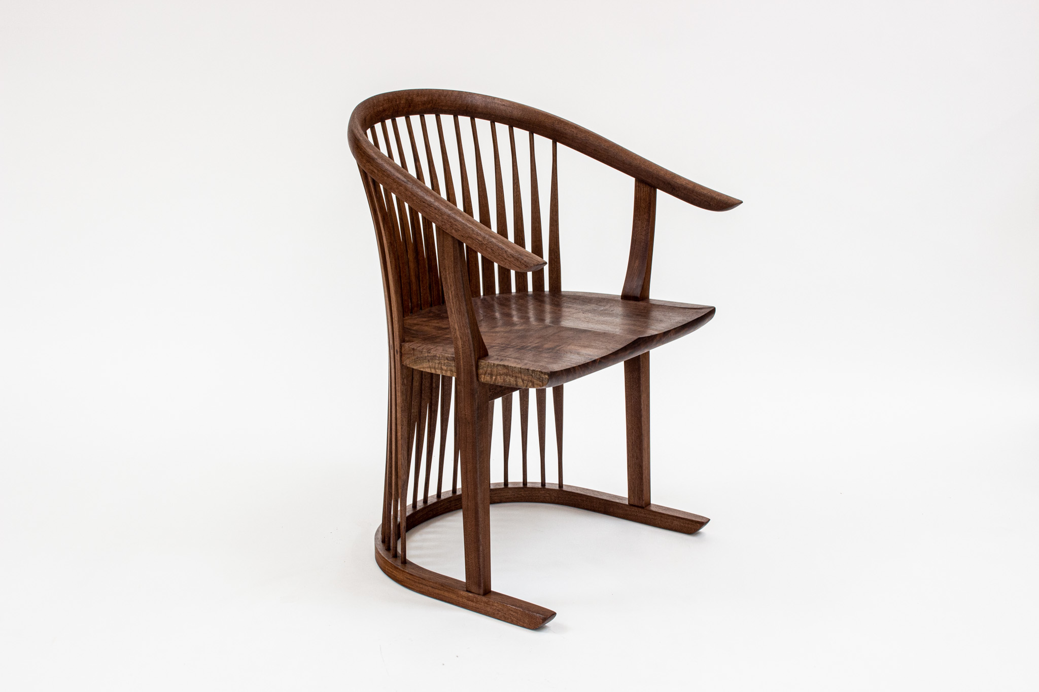 Three quarter view of a walnut Tricot Chair by artist Matt Essex, 2023, with curved legs and arms