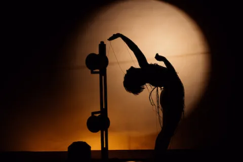 Silhouette of dancer leaning backwards towards an object behind her