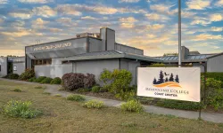 Photo of the front exterior of the Coast Center with signage and landscaping in front, setting sun and clouds in the background. 